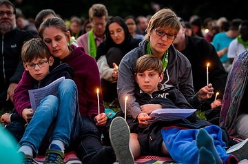 Frauen sitzen mit Kindern mit brennenden Kerzen zwischen anderen Menschen auf einer Wiese, bei der "Nacht der Lichter", am 21. Juni 2019 auf dem Deutschen Evangelischen Kirchentag (DEKT) in Dortmund.