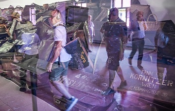 Besucher spiegeln sich im Glas, hinter dem Koffer von Häftlingen ausgestellt sind, in einem Ausstellungsraum der KZ-Gedenkstätte Auschwitz I (Stammlager), am 22. September 2023 in Oswiecim (Polen).