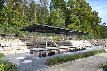 Essen und Trinken auf dem Friedhof: Großer Steintisch mit Sitzgelegenheiten und Sonnenschirmen am 18. Oktober 2023 auf dem "Campus Vivorum" in Süßen.