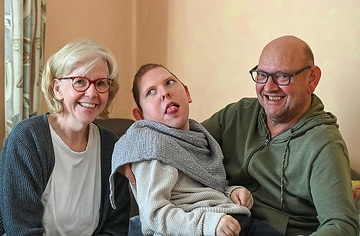 Margret und Günter Gasper halten am 7. November 2023 ihren Sohn Daniel in den Armen auf dem Sofa zuhause in ihrer Wohnung in Alfter.