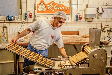 Ein Bäcker steht mit einem Backblech mit aus Teig ausgestanzten Printen an einer Maschine am 30. Oktober 2023 in der Printenbäckerei Klein in Aachen.