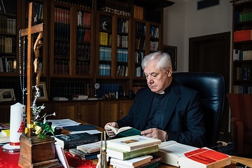 Kardinal Gerhard Ludwig Müller sitzt am 18. Februar 2019 am Schreibtisch und liest ein Buch in seiner Wohnung in Rom. Auf dem Schreibtisch steht ein Kruzifix, an dem ein Rosenkranz hängt.