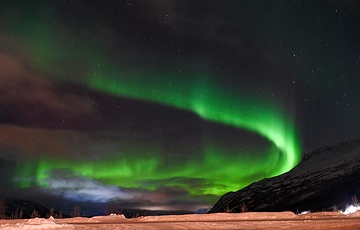 Nordlicht leuchtet grün am dunkelblauen Nachthimmel über einem Berg in der Nähe von Alta (Norwegen) am 12. Dezember 2023.