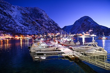 Kleine Fischerboote sind beleuchtet am 13. Dezember 2023 im Hafen von Oksfjord (Norwegen). Das wenige Tageslicht ist blau-violett.