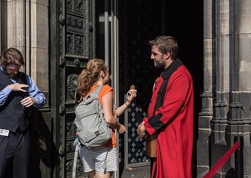Ein Domschweizer im kontrolliert am 2. August 2018 eine Touristin am Haupteingang des Kölner Doms.