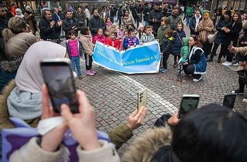 Kinder halten ein Banner mit der Aufschrift "Blühende Integration Taunus e.V.", Menschen fotografieren mit ihren Smartphones, bei der erstmaligen Illumination mit Lichterschmuck zum islamischen Ramadan Fest in der Freßgass in Frankfurt am 11. März 2024.