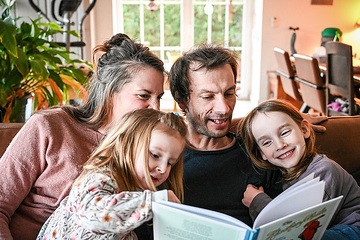 Mutter, Vater, Tochter und Sohn (r.) sitzen am 6. März 2024 auf dem Sofa zuhause in Rheinbach. Der Vater liest den Kindern vor aus dem Buch "Die Häschenschule".