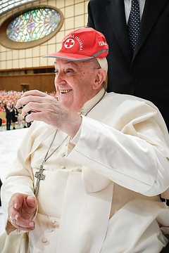 Papst Franziskus scherzt mit einer Kappe des Roten Kreuzes auf dem Kopf am 6. April 2024 in der Audienzhalle im Vatikan bei einem Treffen mit ehrenamtlichen Mitarbeitenden des Roten Kreuzes in Italien.