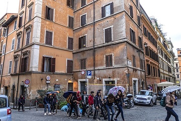 Jugendliche laufen auf der Straße mit Regenschirmen in der Via Rasella in Rom am 13. März 2019. In der Hausfassade sind Löcher, da in der Via Rasella während des Zweiten Weltkriegs eine von Partisanen gelegte Bombe detonierte und die Schäden noch nicht beseitigt wurden.