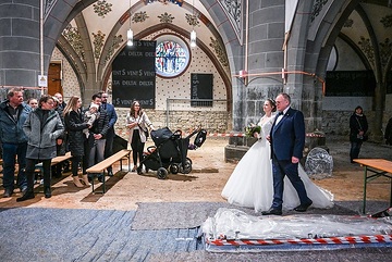 Der Brautvater führt die Braut zu Beginn des Gottesdienstes zum Altar am 20. April 2024 in der Kirche Sankt Laurentius in Bad Neuenahr-Ahrweiler. Sie gehen über ein Malervlies an abgesperrten Bodenarbeiten vorbei.