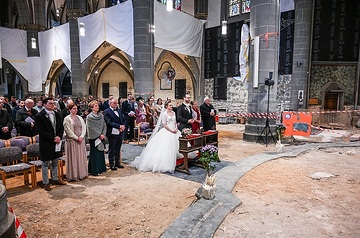 Ein Hochzeitspaar steht in der Kniebank in der Mitte bei einer Trauung am 20. April 2024 in der Kirche Sankt Laurentius in Bad Neuenahr-Ahrweiler. Die Kirche ist eine Baustelle, Trockner und Absperrbänder sind zu sehen, der Boden ist staubige trockene Erde.