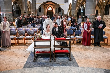 Ein Hochzeitspaar sitzt auf Stühlen in der Mitte bei einer Trauung am 20. April 2024 in der Kirche Sankt Laurentius in Bad Neuenahr-Ahrweiler. Die Kirche ist eine Baustelle, Trockner und Absperrbänder sind zu sehen, der Boden ist staubige trockene Erde.